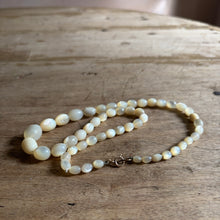 Laden Sie das Bild in den Galerie-Viewer, A strand of round, polished beads in a creamy off-white color, arranged on a rustic wooden surface. The beads have a smooth, lustrous finish and are joined by a small silver-toned lobster clasp.