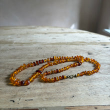 将图片加载到图库查看器，A handmade amber bead necklace with a small antique bronze clasp, resting on a rustic light-colored wooden surface.
